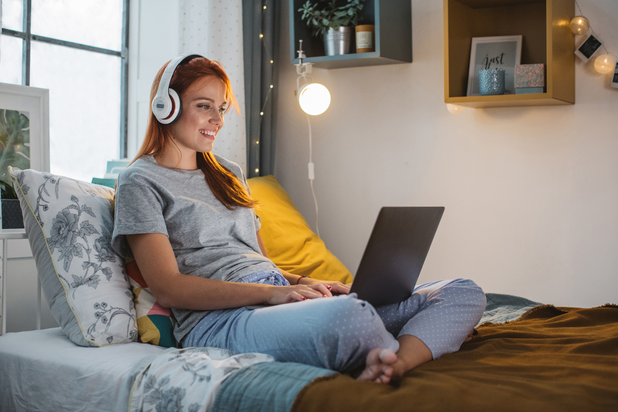 Frau fröhlich im Bett vorm Laptop